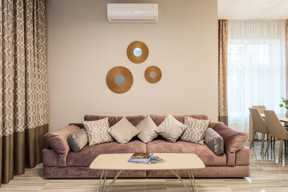 A tastefully decorated living room featuring a plush dusty rose sofa adorned with five decorative cushions in shades of beige and gray. In front of the sofa, there is a white rectangular coffee table 